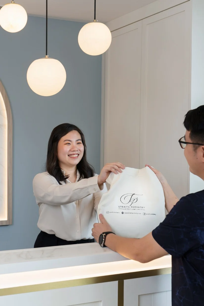 Receptionist assisting patient of Straits Podiatry at the counter.